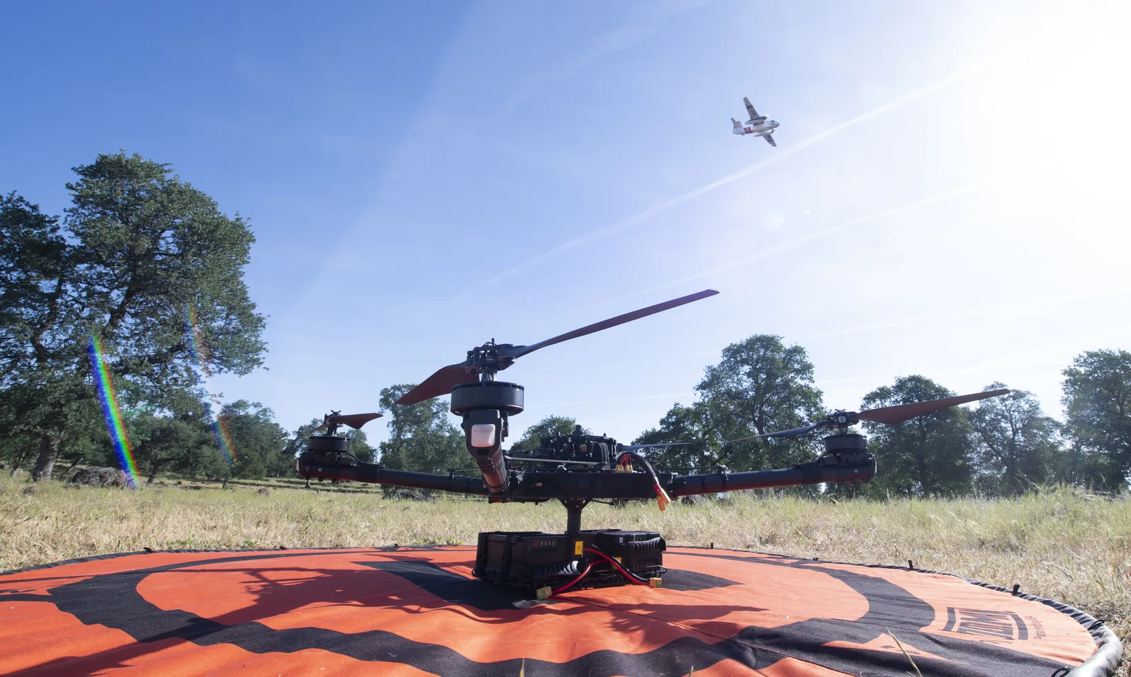 A firefighting airtanker flying past a hovering multirotor drone.