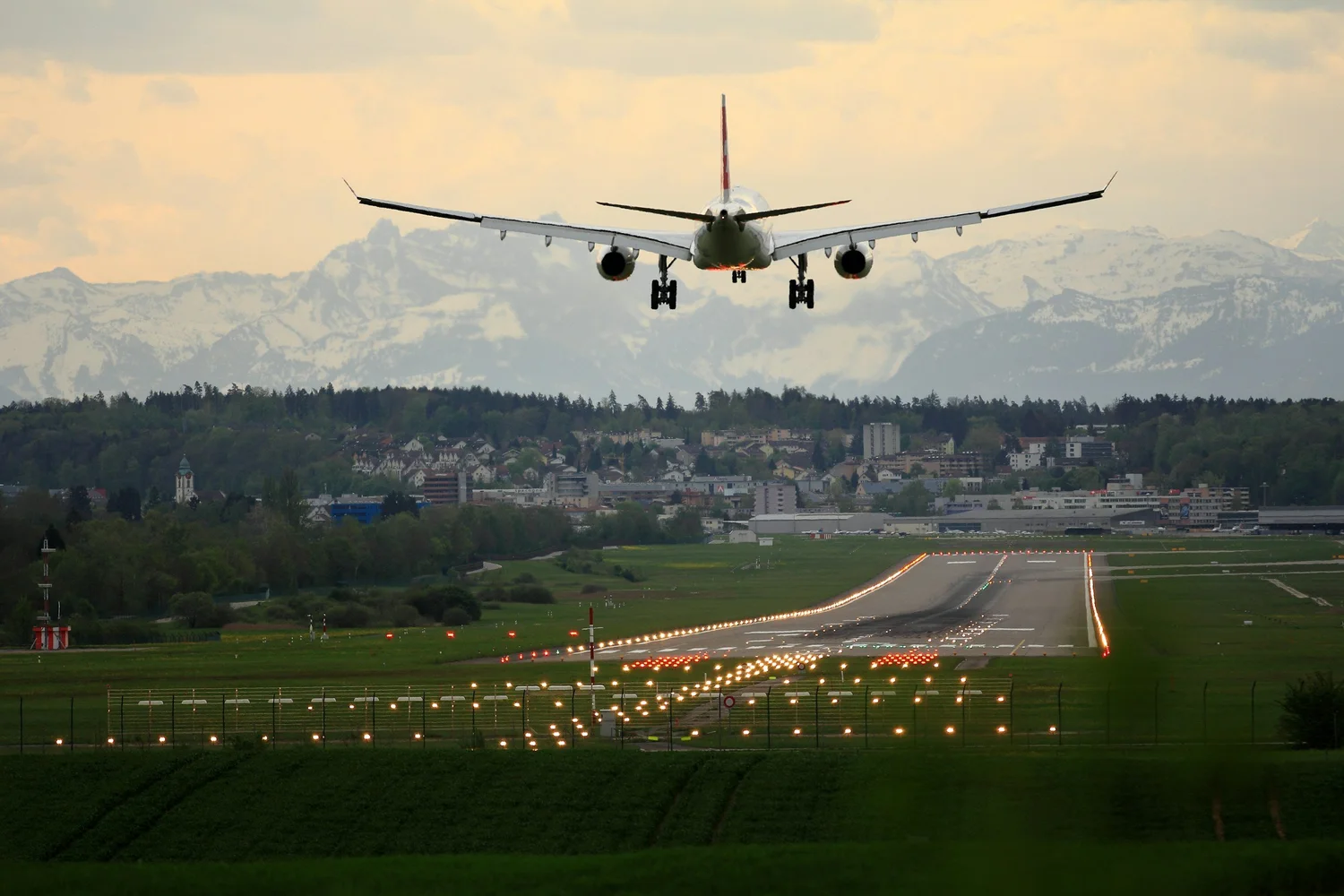 A commercial airliner on final approach over a lit runway at dusk.
