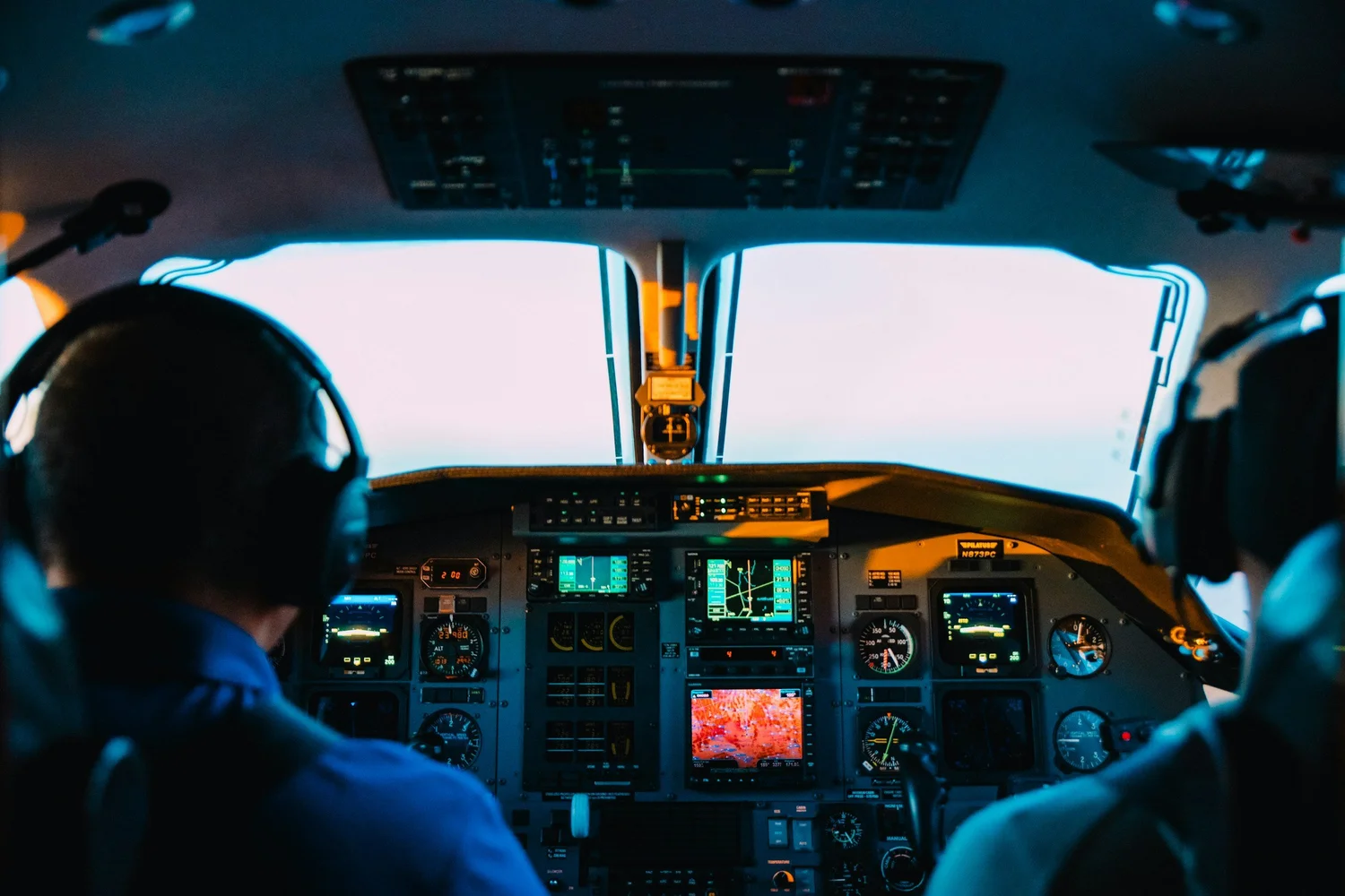 The flight deck of an aircraft at dusk, pilots at the controls.