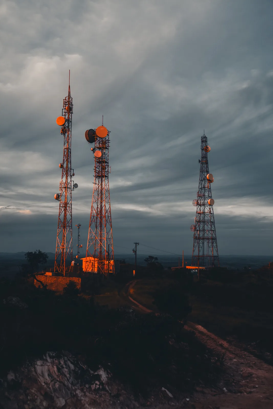 Silhouetted radio masts against a dramatic overcast sky at dusk.