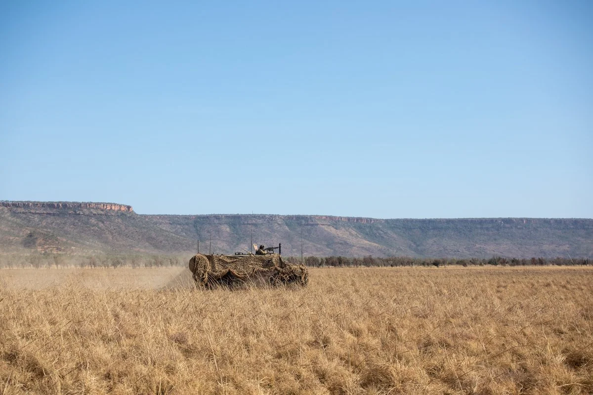 A camouflaged armoured vehicle moving across open plains during a military exercise.