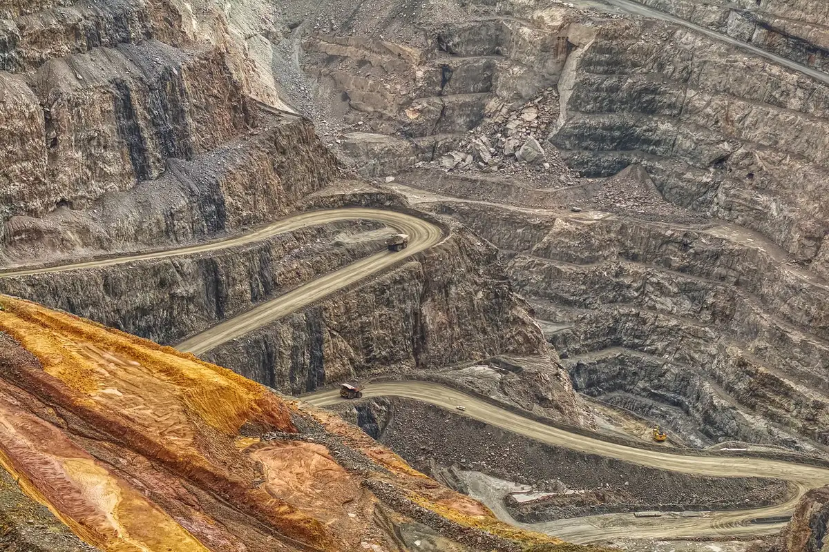 Aerial view of haul trucks on switchback roads cut into the wall of an open pit.