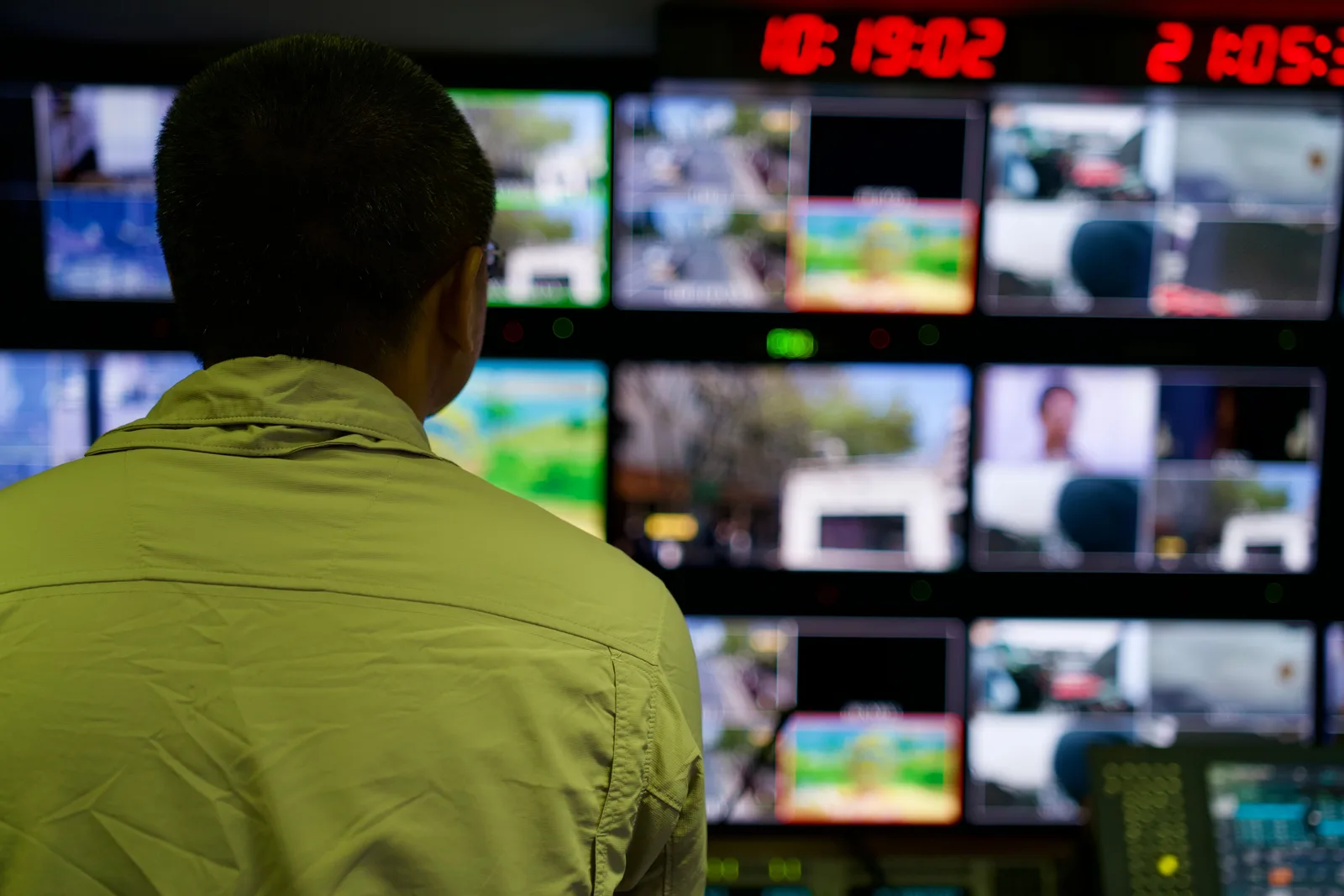 An operator watching a wall of monitors in a darkened control room.