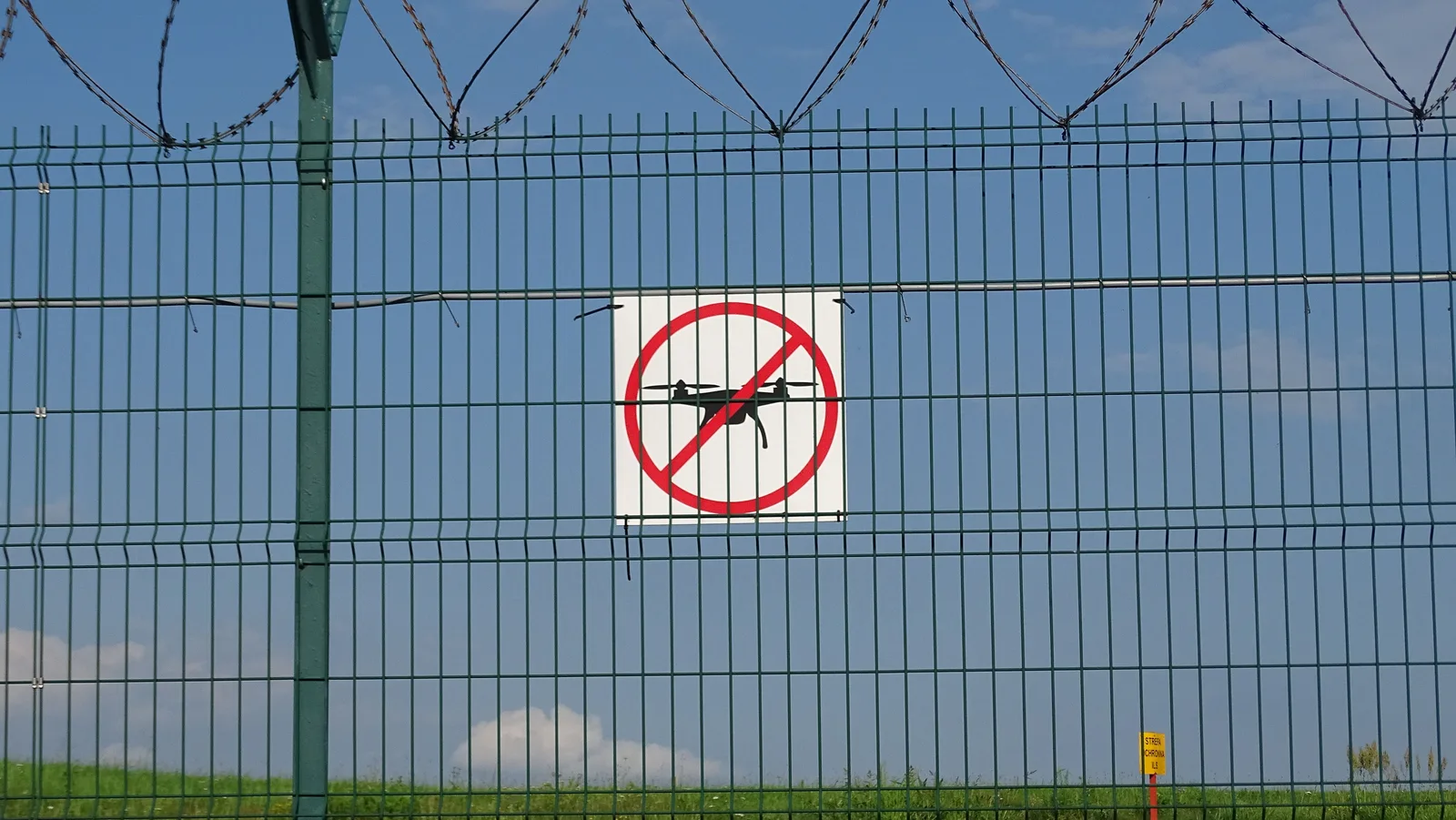 A drone-prohibition sign fixed to a barbed-wire fence.