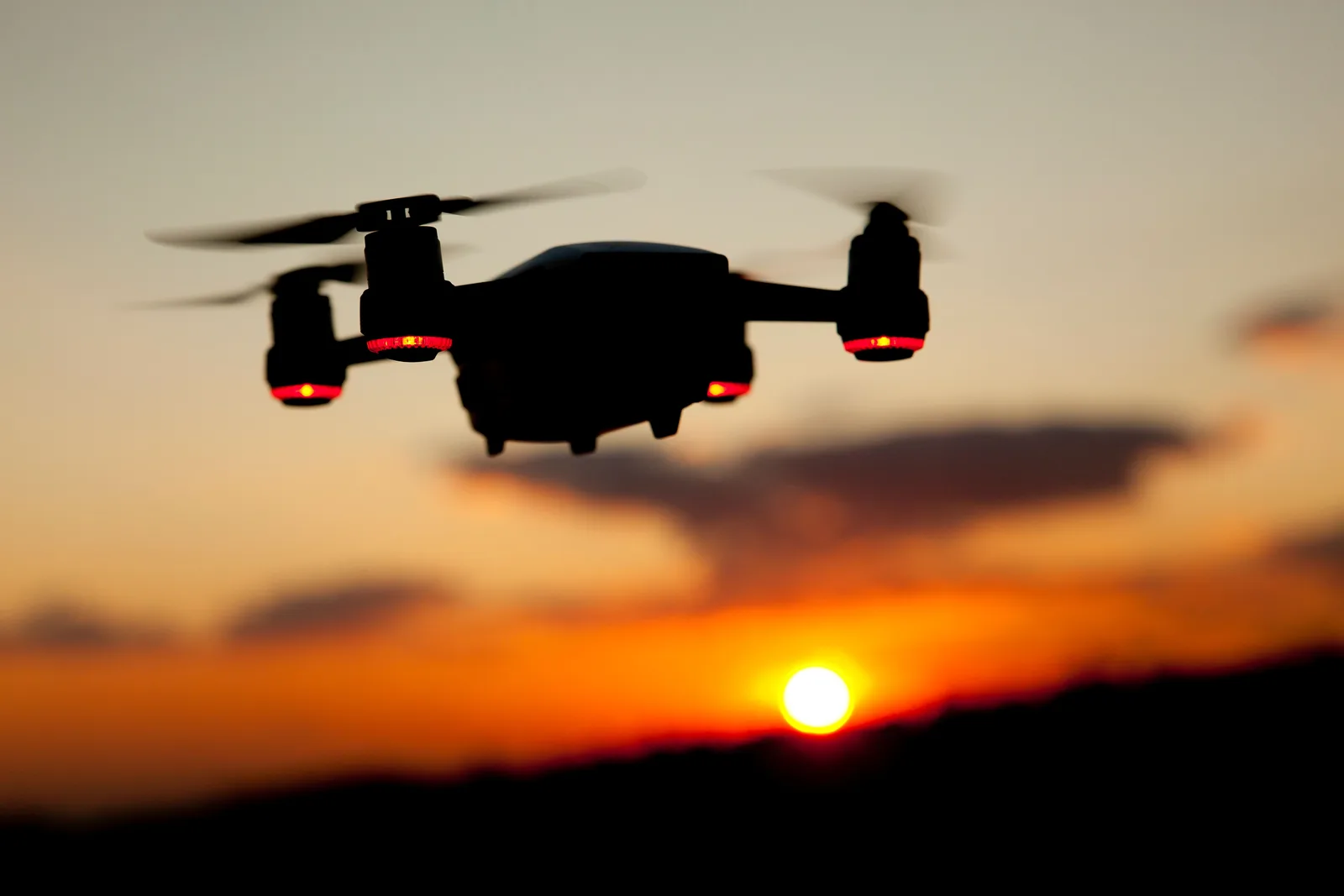 The silhouette of a quadcopter drone against a sunset sky.