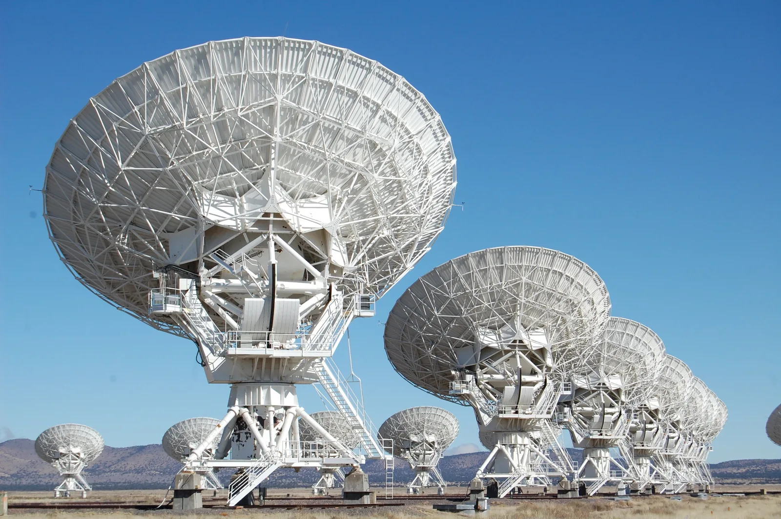 A rank of parabolic dish antennas stretching across open plains.