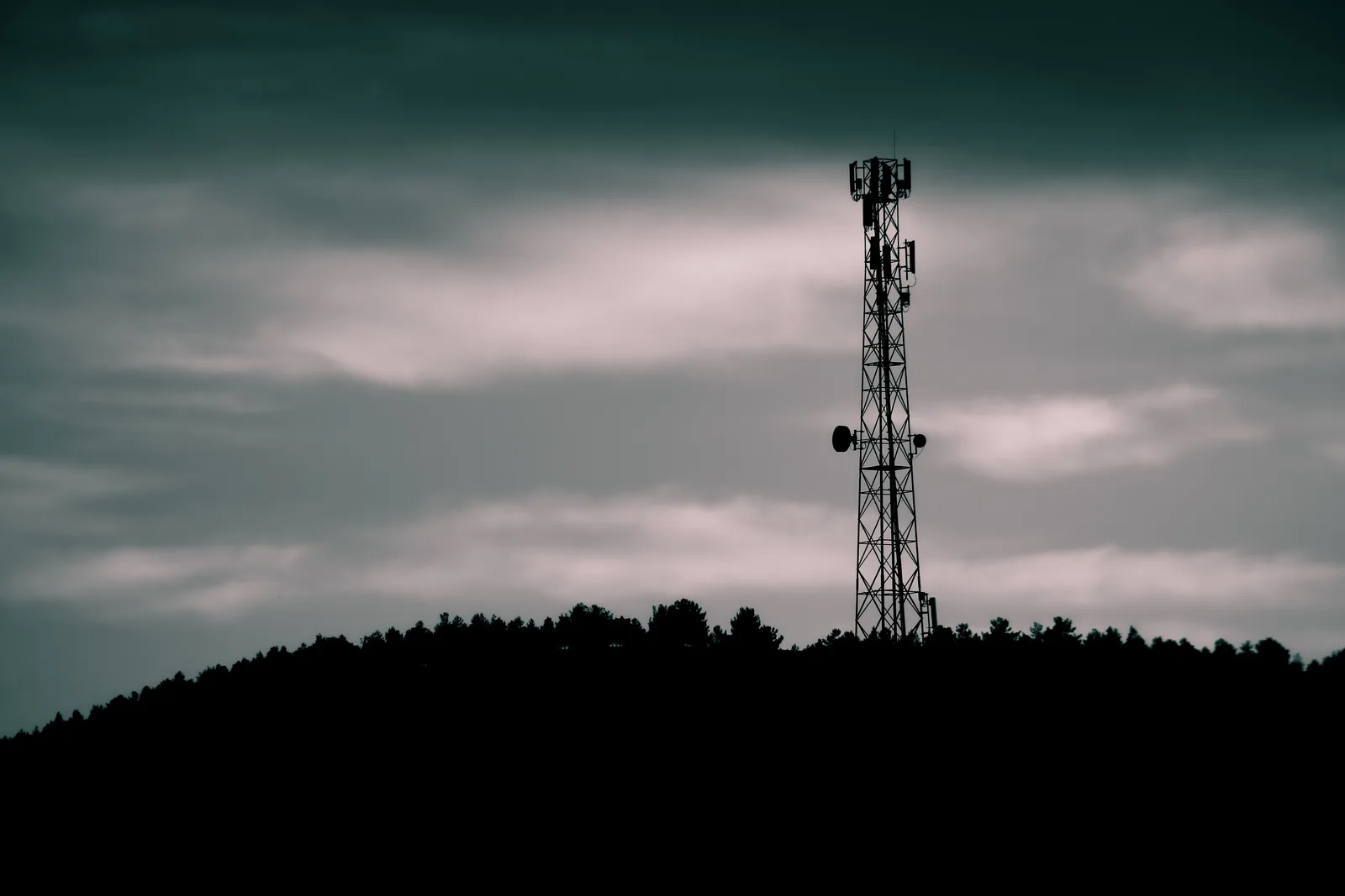 A telecommunications tower with panel antennas silhouetted under a night sky.